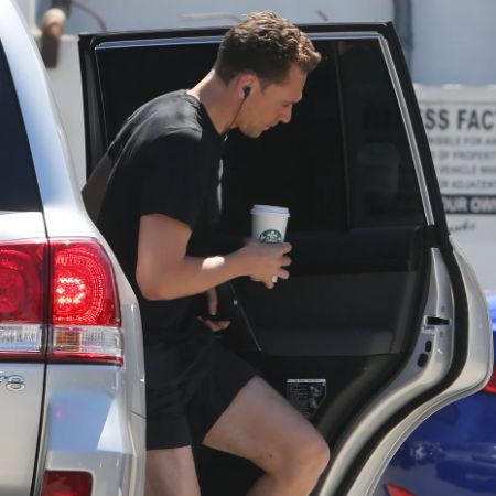Tom Hiddleston with a earphone in his ear comes out from the car
